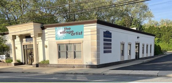 A white building with a red awning that says the village artist