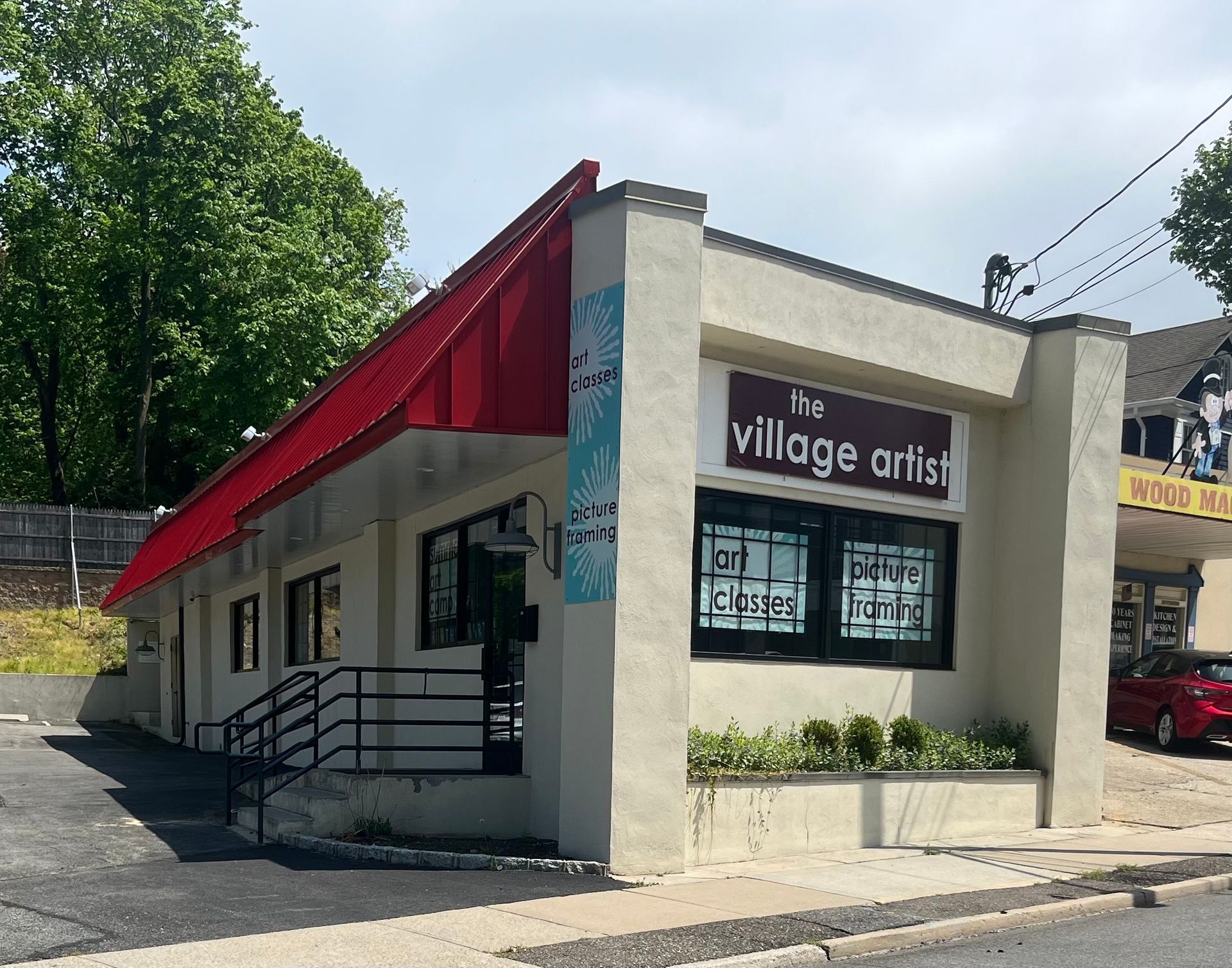 A white building with a red awning that says the village artist