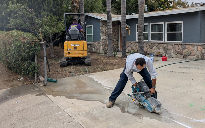 Drainiacs Sewer & Drain working on a mainline with an excavator and cement saw.