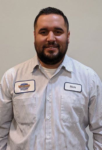 Man in a striped shirt, wearing a name tag. He is smiling and has a beard.