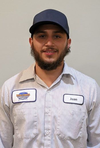 Man wearing a cap and work shirt, with a name tag. He has a beard and is smiling.