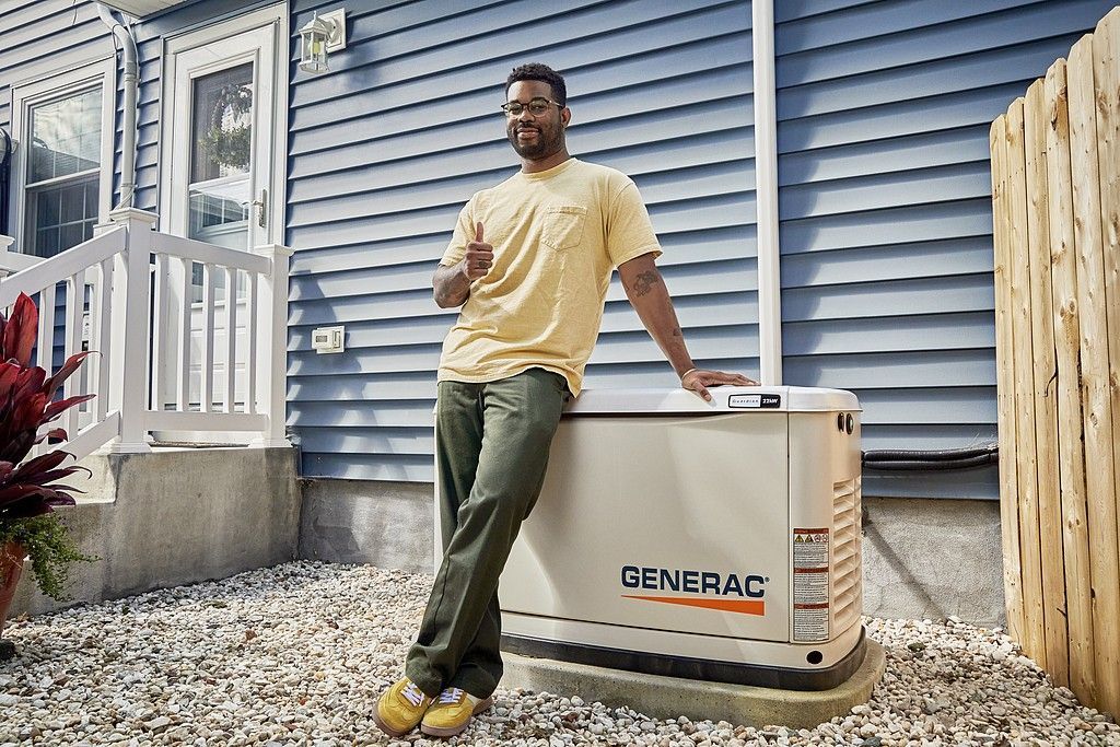 A man is leaning on a generator outside of a house.