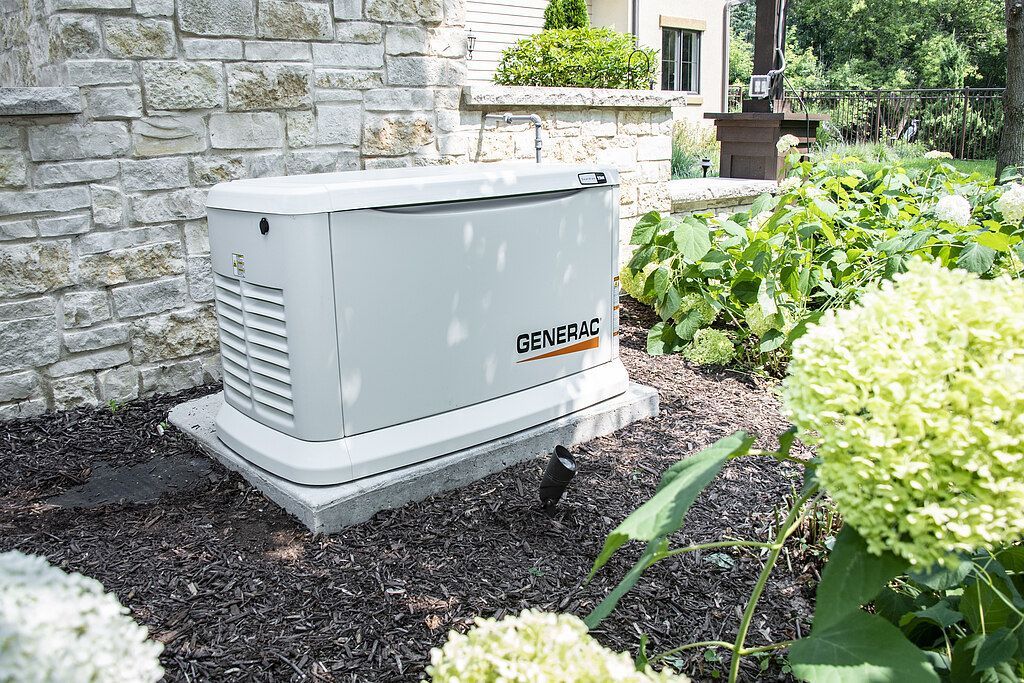A generator is sitting in a garden next to a brick wall.