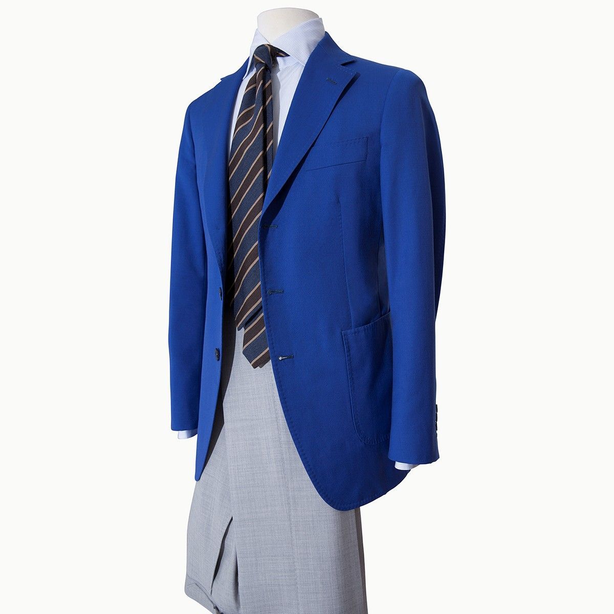 A blue blazer, striped tie, and light grey dress trousers displayed on a mannequin against a white background.