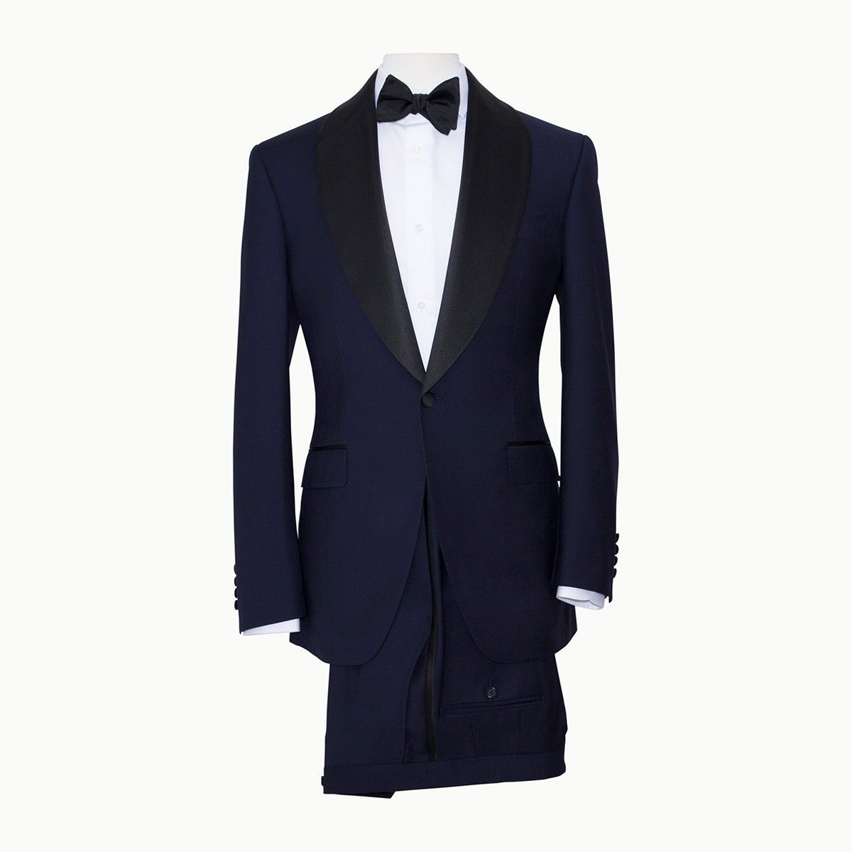 A navy blue tuxedo jacket with black silk shawl lapels, a white dress shirt, and a black bowtie on a mannequin.