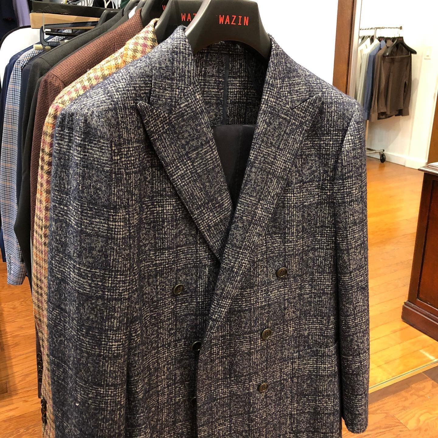 A navy blue, textured double-breasted suit jacket hangs on a rack in a clothing store.
