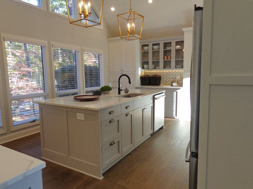 A kitchen with white cabinets, a large island, a sink, and a refrigerator.