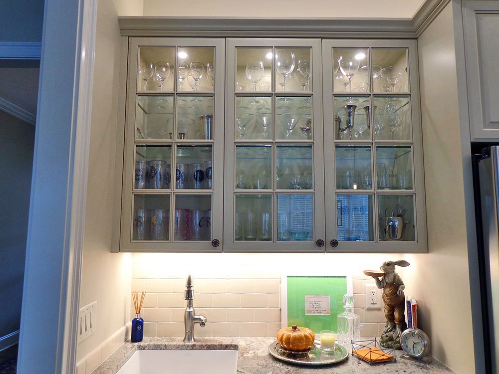 A kitchen with a sink and a glass cabinet filled with wine glasses.