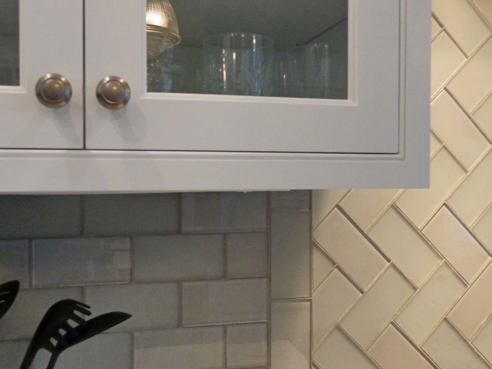 A kitchen with white cabinets and a herringbone tile wall.