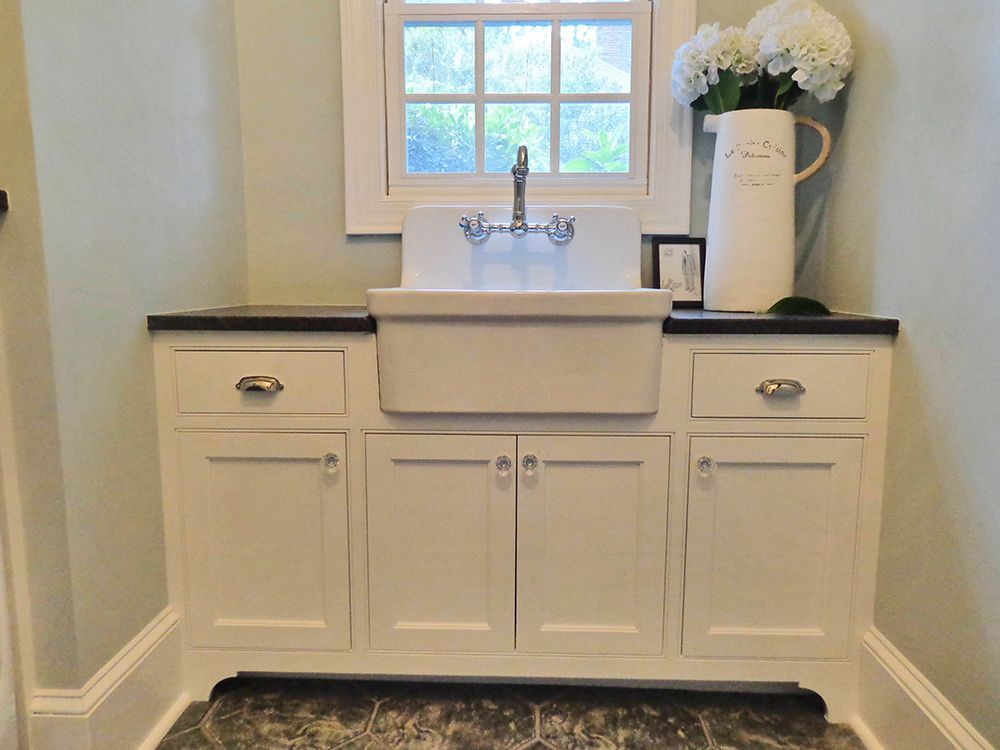 A laundry room with white cabinets and a sink.