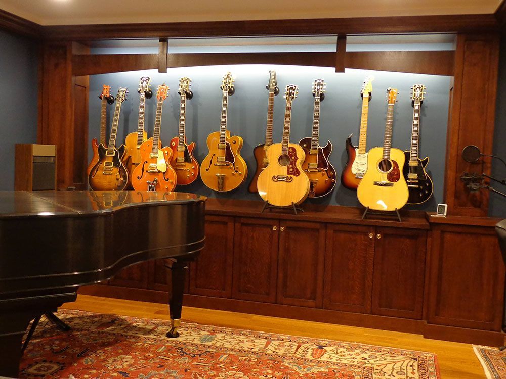A room with a piano and many guitars on the wall.