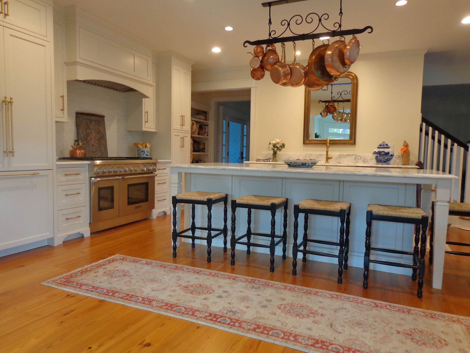A kitchen with stools and copper pots hanging from the ceiling