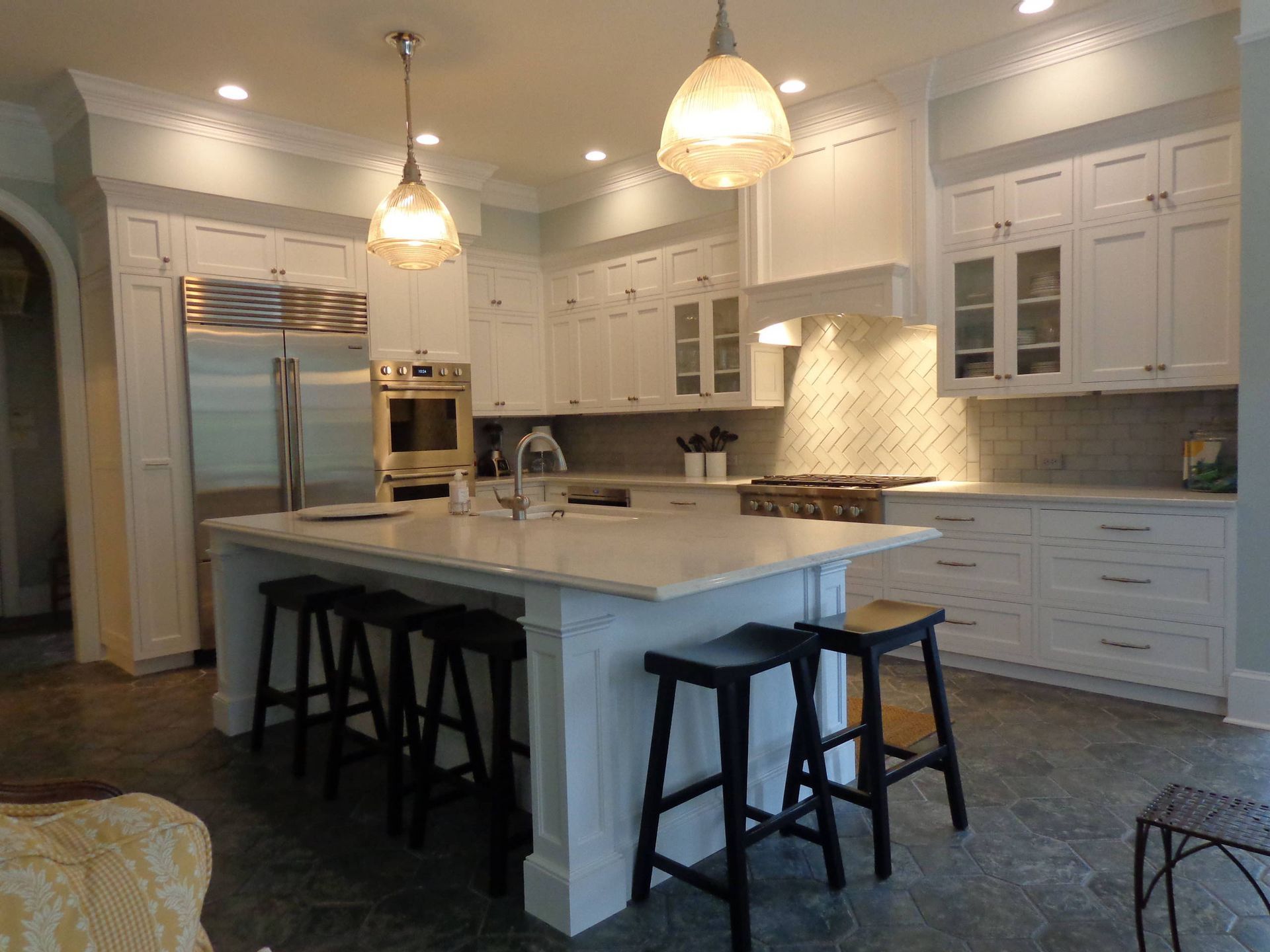 A kitchen with white cabinets and stools and a large island in the middle.