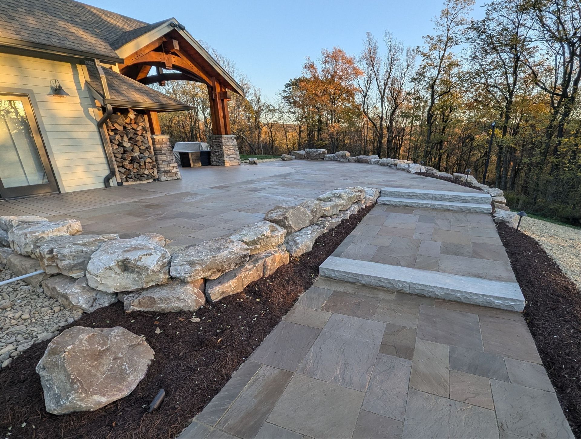 A stone walkway leading to a house with a wooden gazebo in the background.