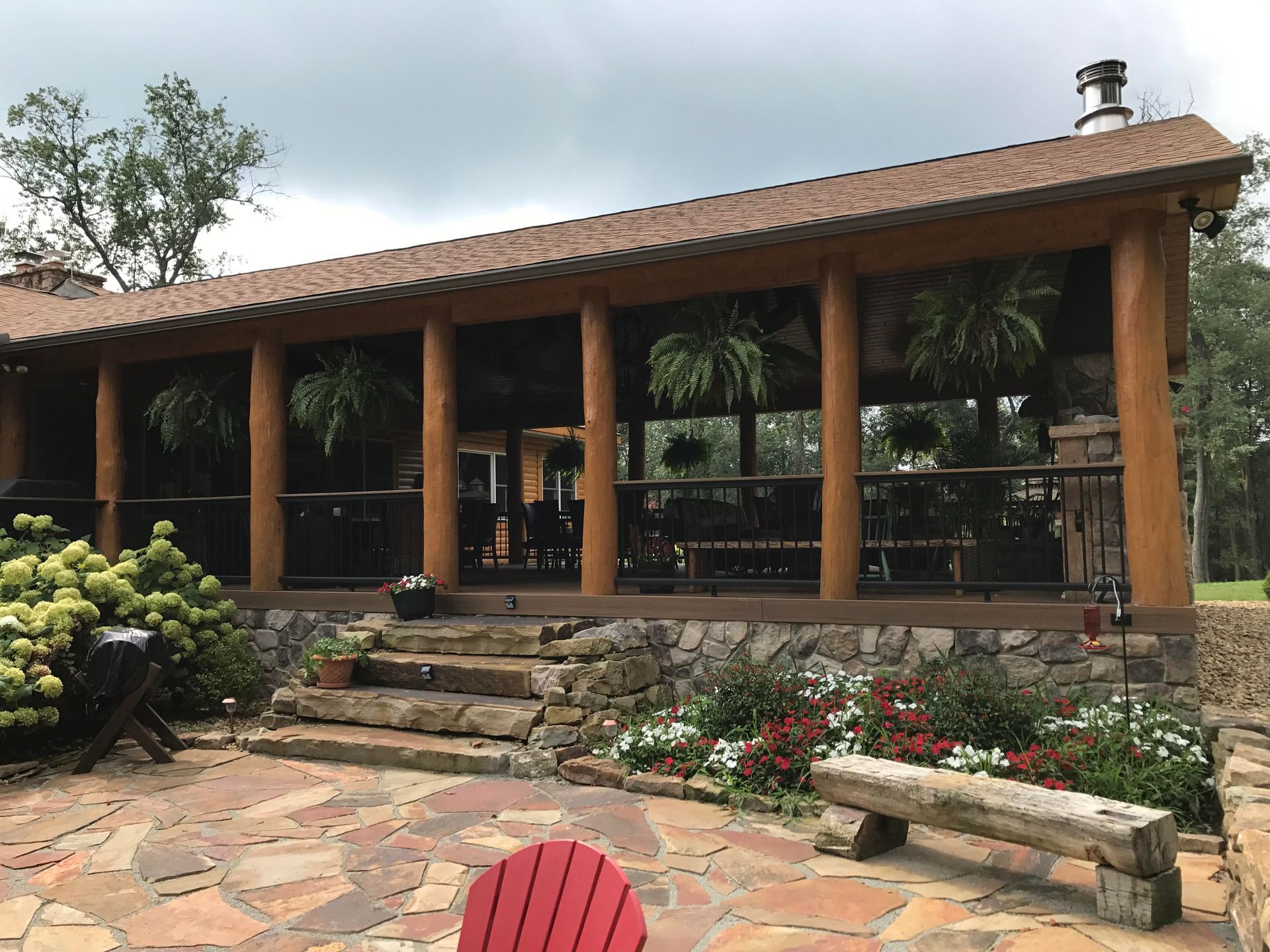 A large wooden building with a stone patio and a red chair in front of it.