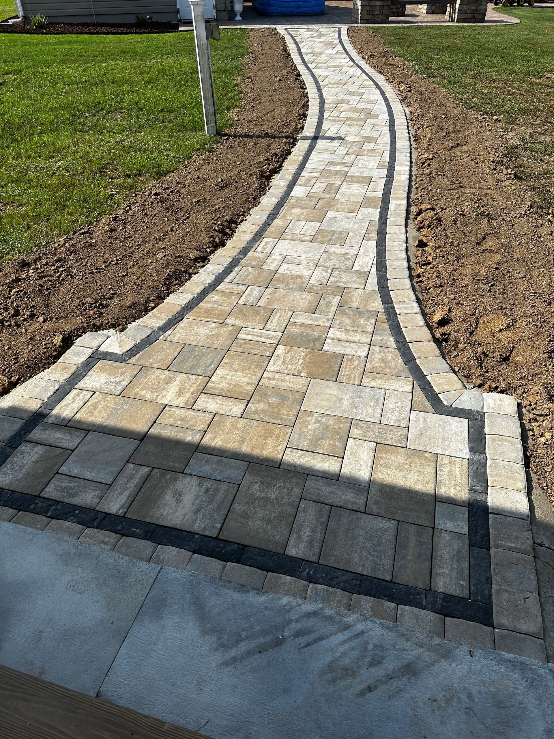 A walkway made of bricks is going through a yard.