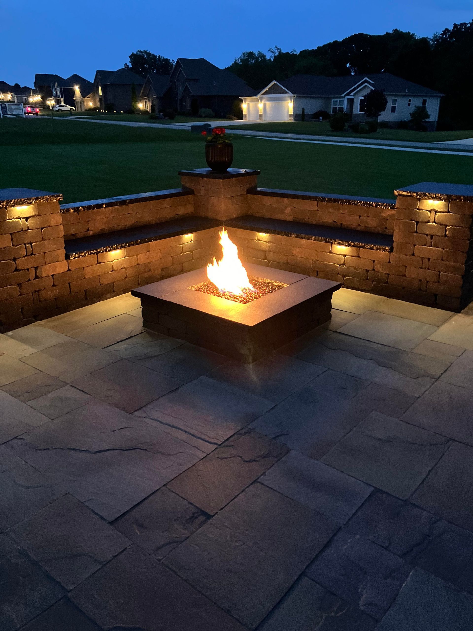 A fire pit is lit up at night in front of a brick wall