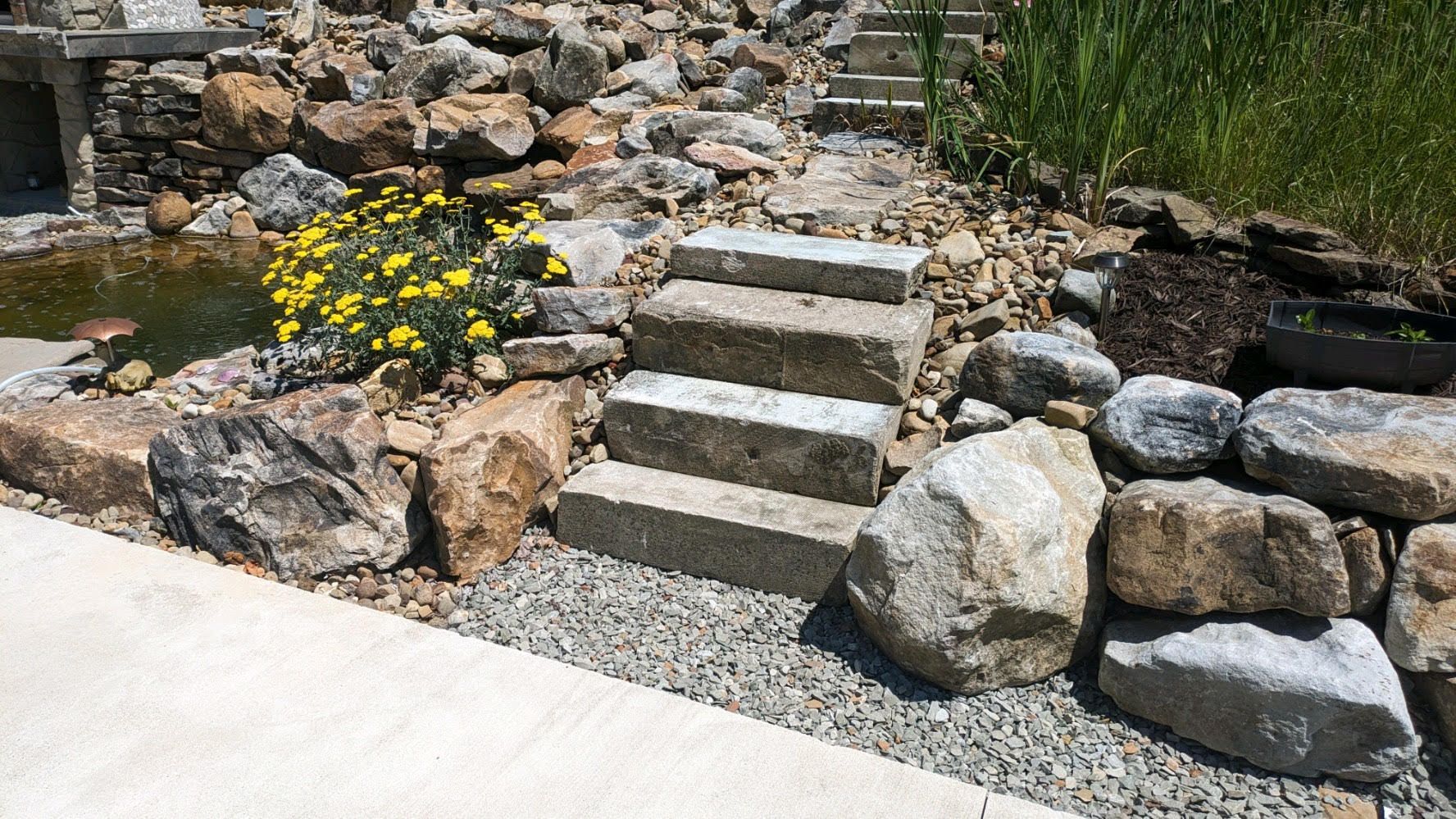 A stone walkway leading to a pond surrounded by rocks and flowers