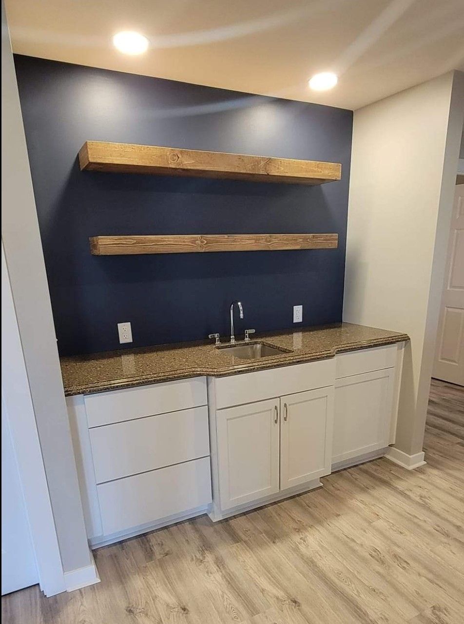 A kitchen with a sink , cabinets , shelves and a blue wall.