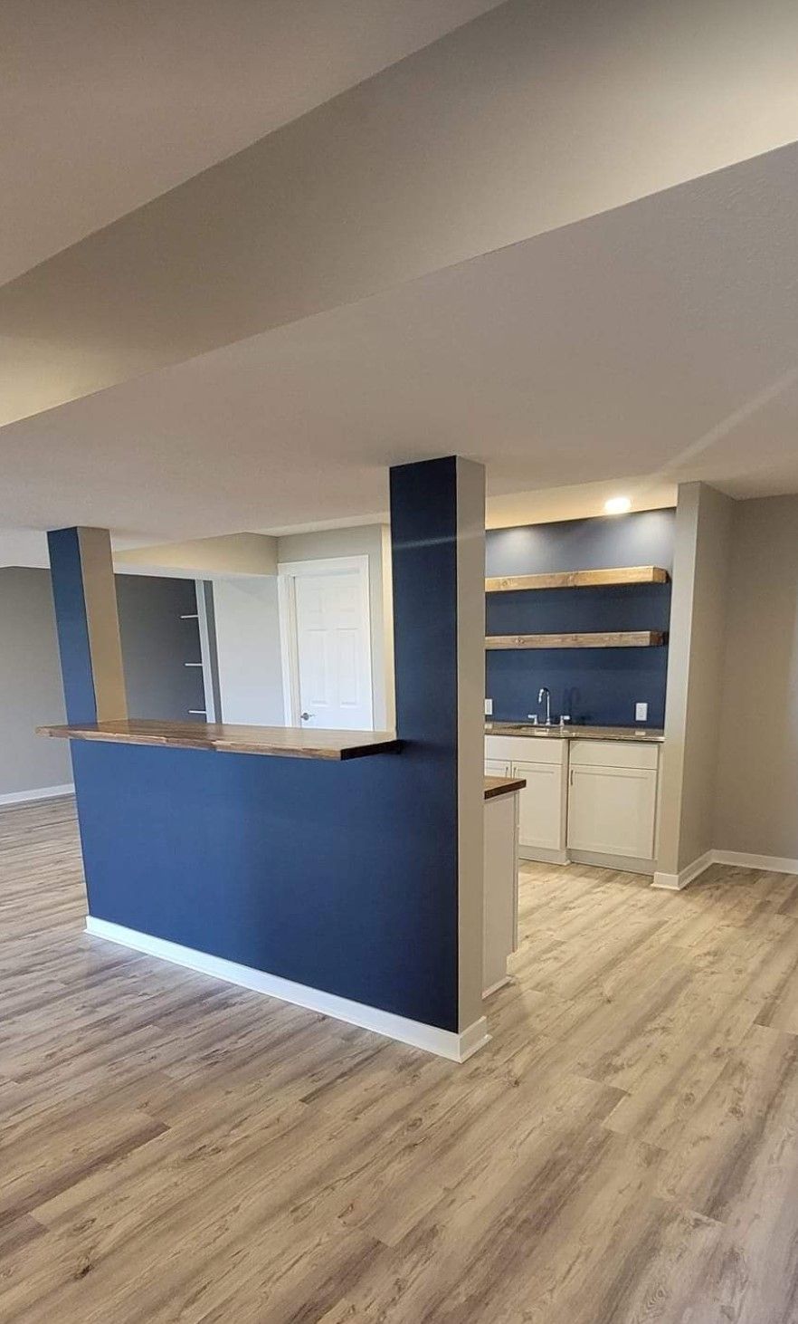 A kitchen in a basement with a blue wall and wooden floors.