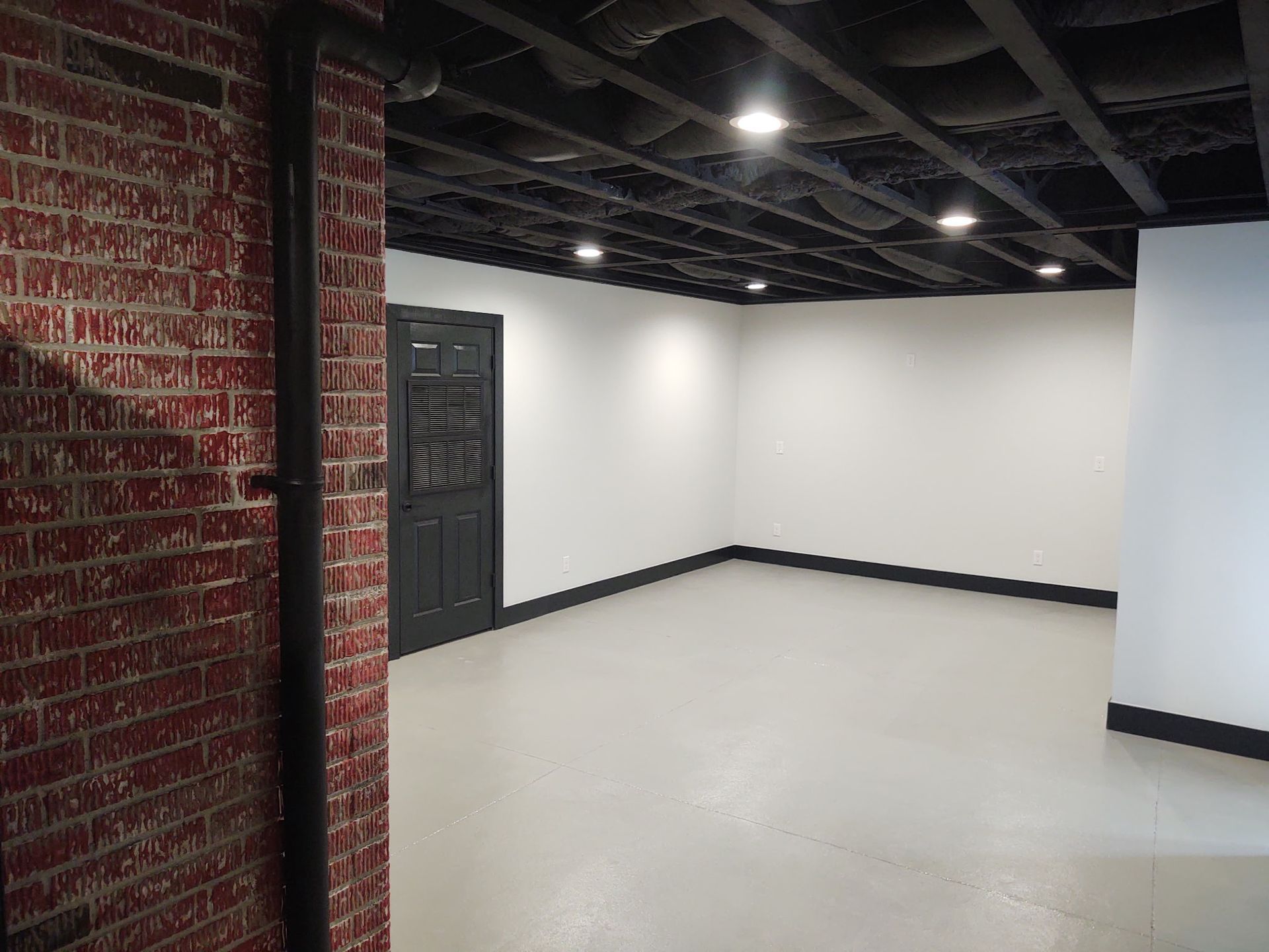 An empty room with a brick wall and a black door.