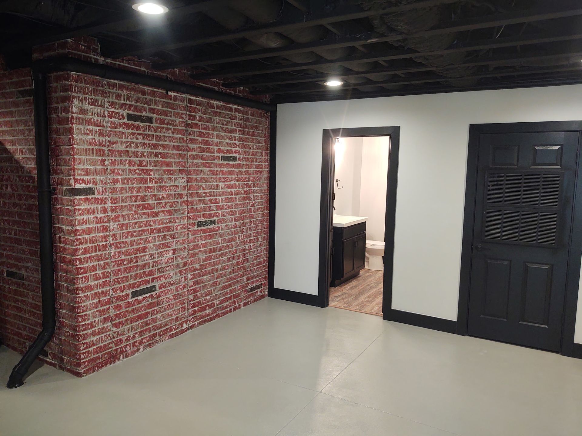 An empty basement room with a brick wall and a black door.