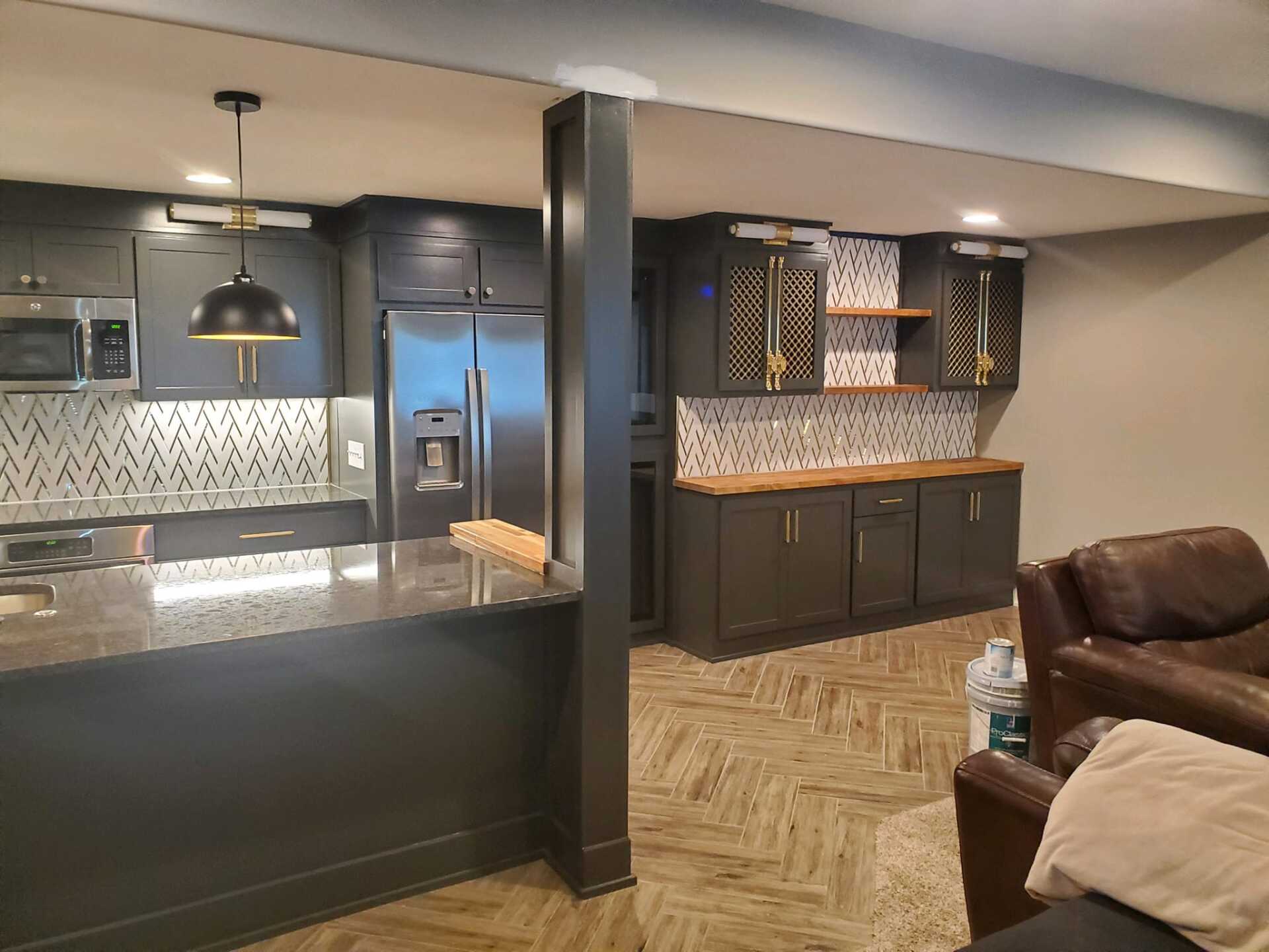 A kitchen and living room in a basement with stainless steel appliances and black cabinets.