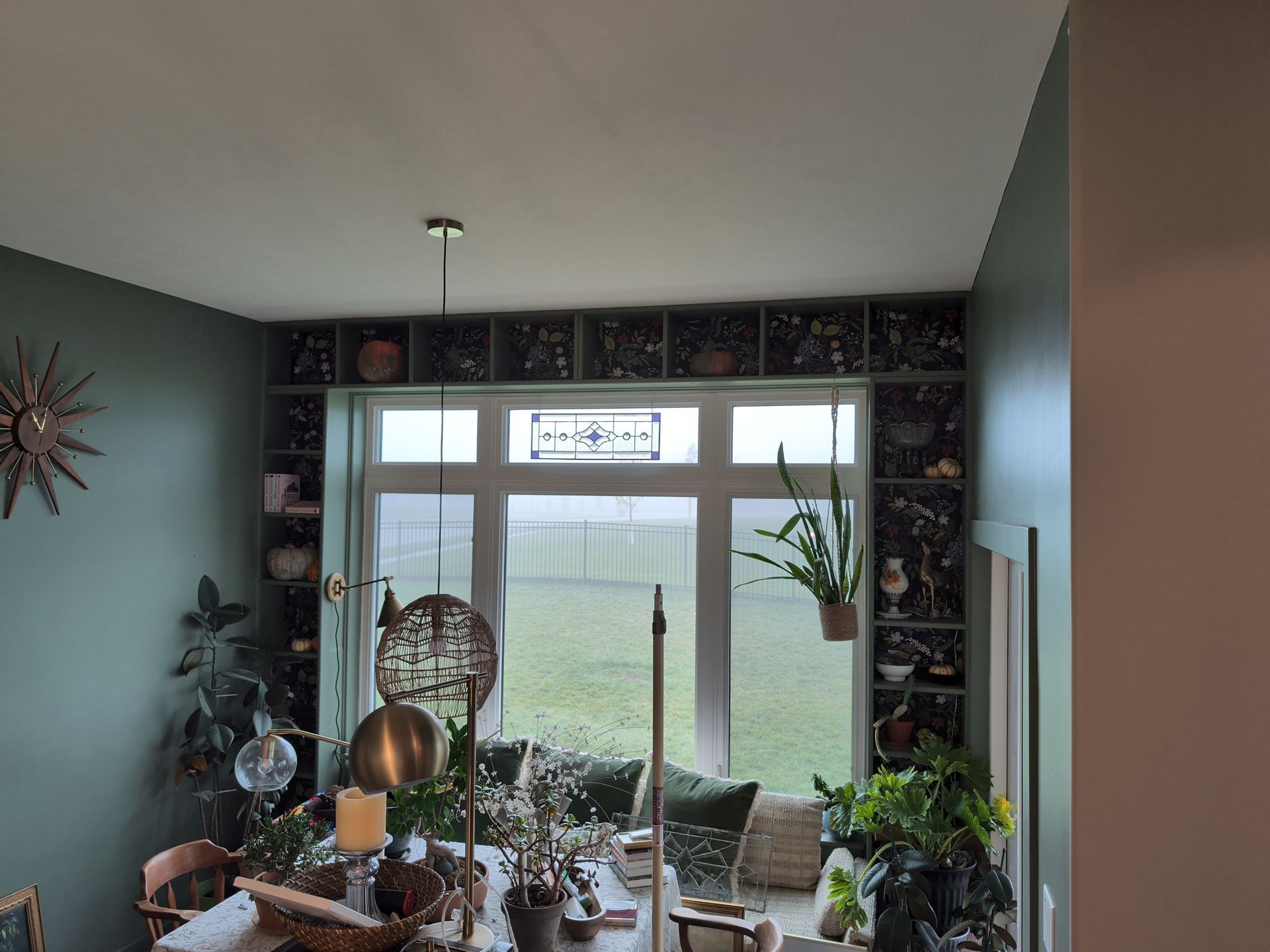 Dining room with built-in shelves, large window, and table set for a meal. Green walls, various plants.