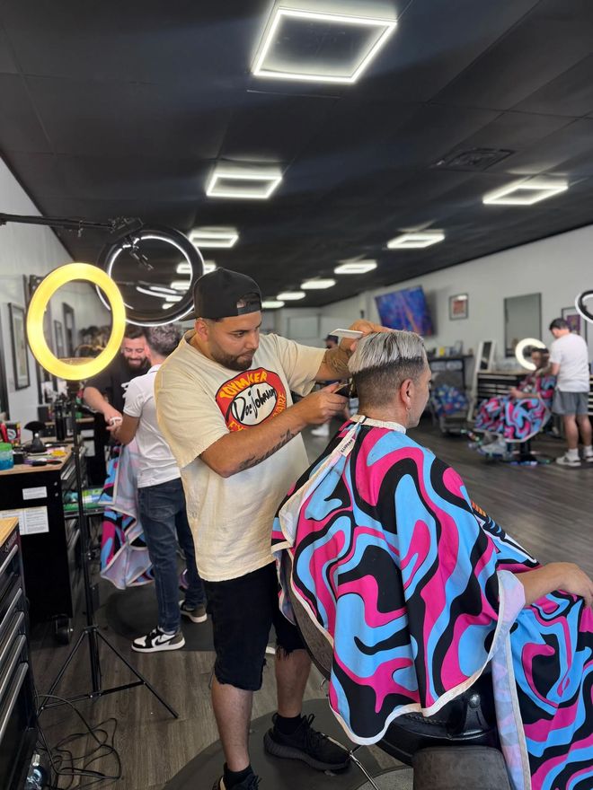 Barber cutting a customer’s hair in a modern barbershop with black ceiling lights and colorful cape