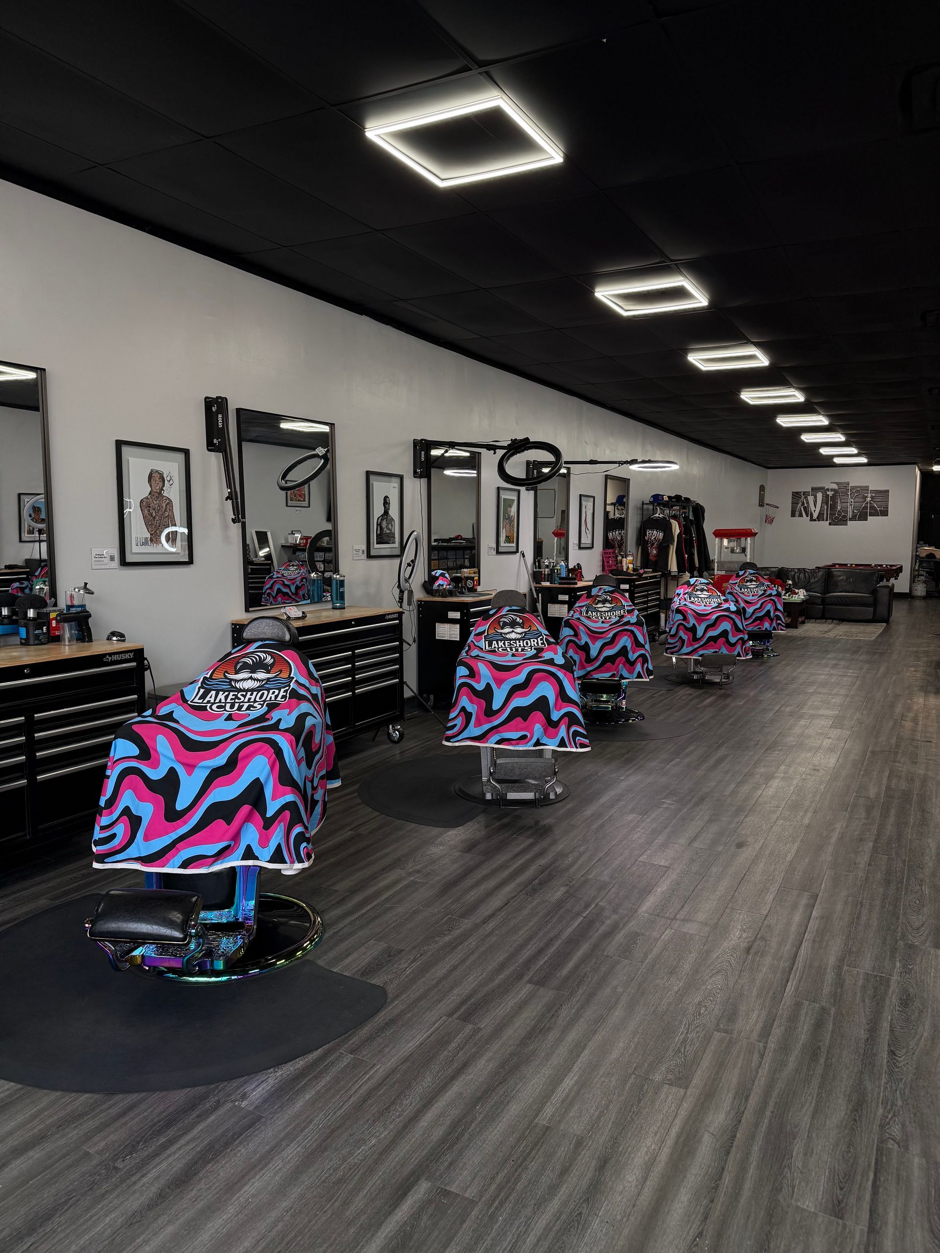 Interior of a modern barbershop with colorful chairs, wall mirrors, and overhead square lights on a dark ceiling.