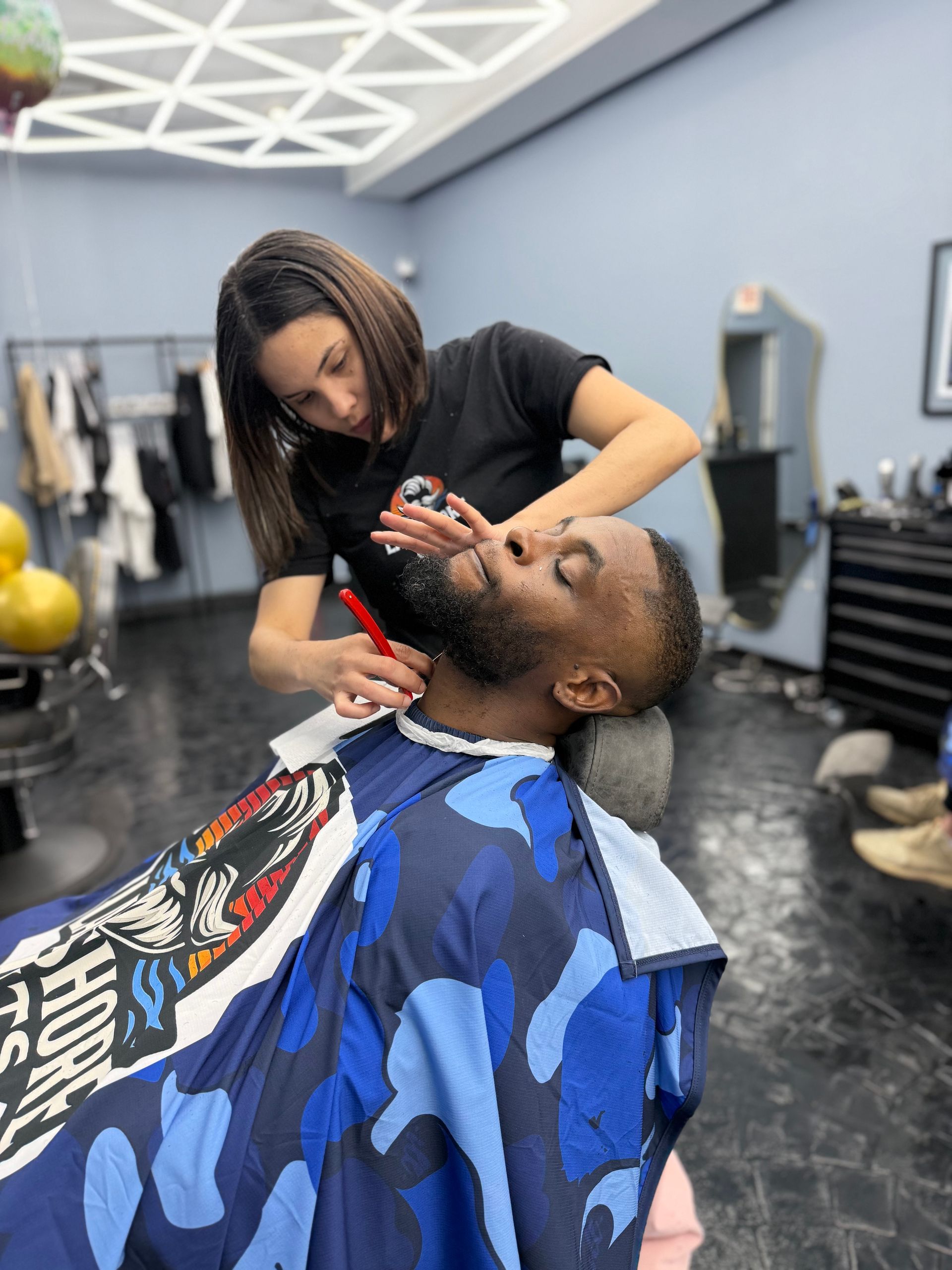 Barber trimming a client’s beard in a modern barbershop, with a blue cape over the client.