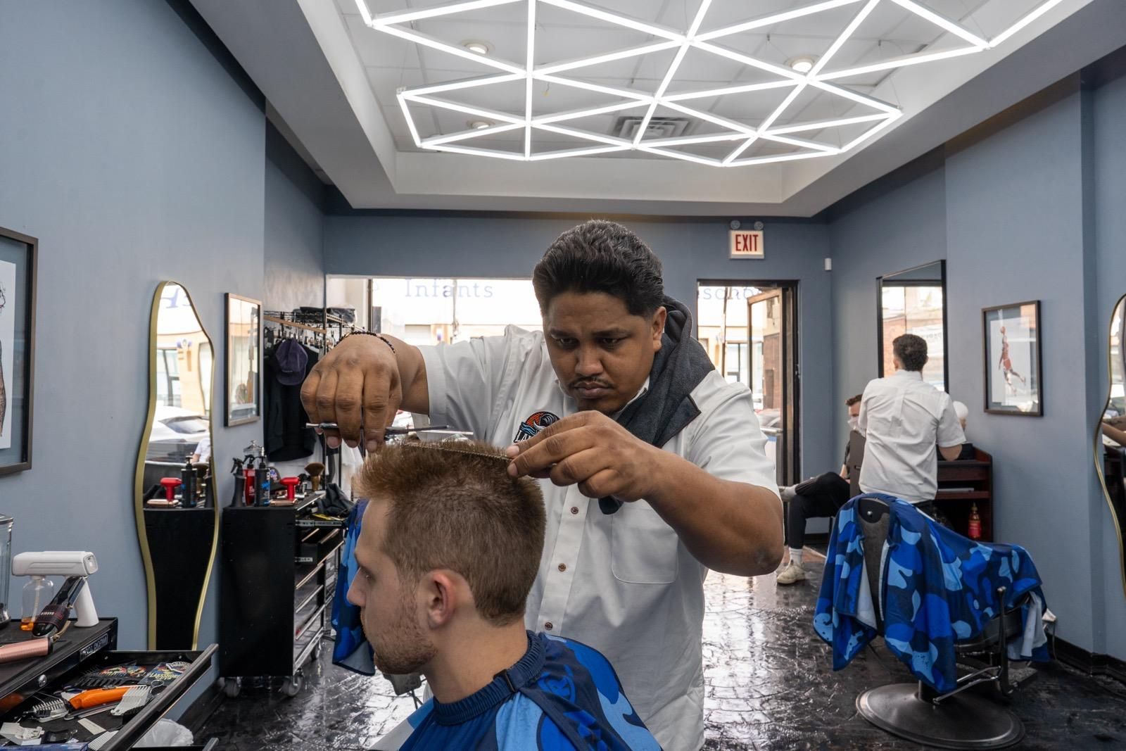 Barber cutting a customer’s hair in a modern salon with geometric ceiling lights and blue chairs