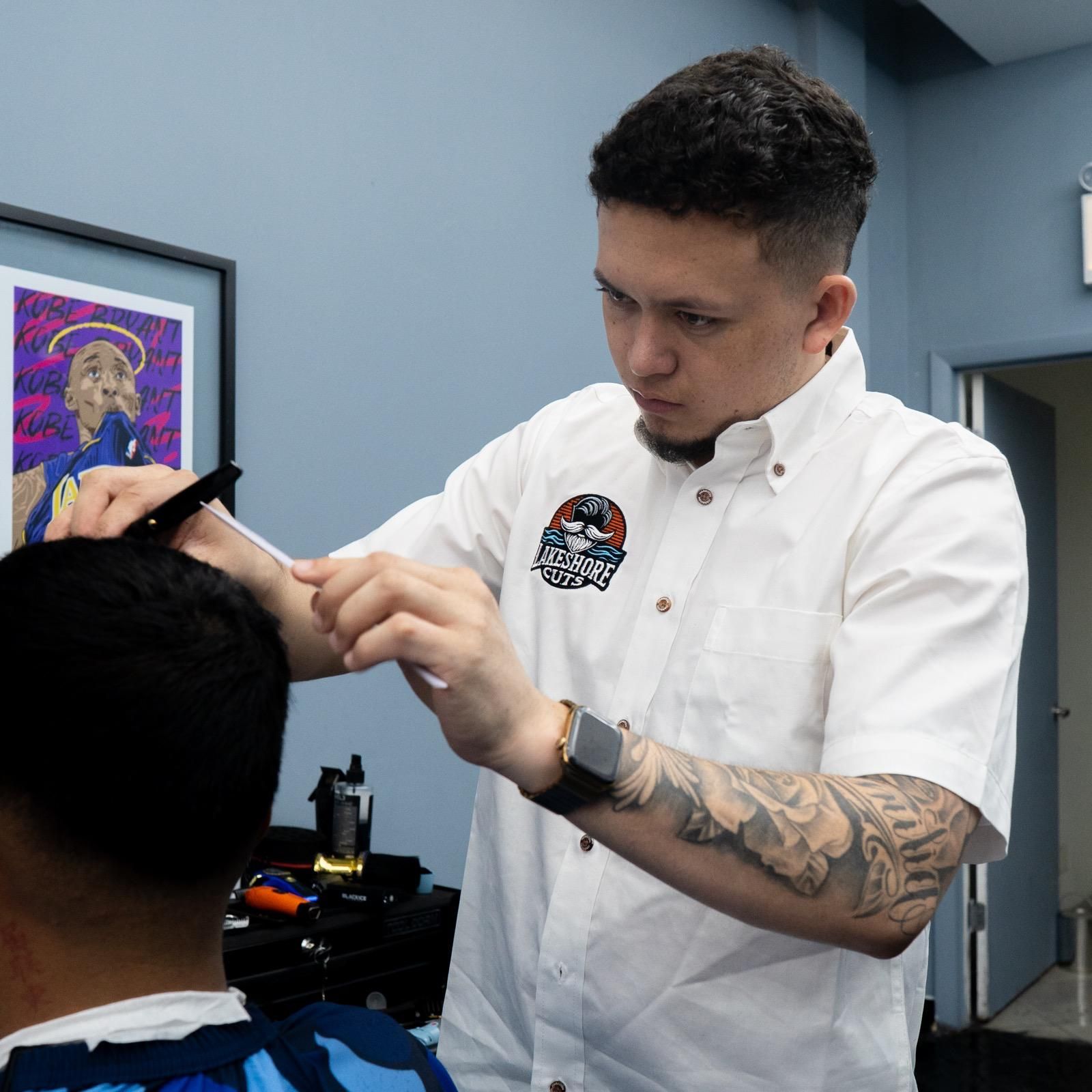 Tattoo artist shaping a client's eyebrow in a studio, with framed art and tools in the background