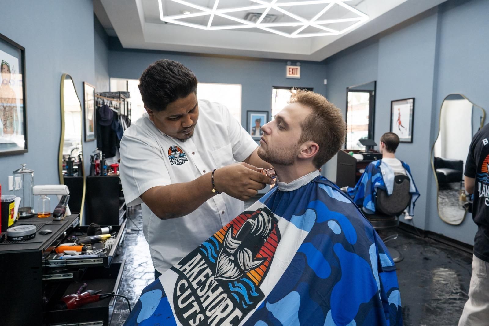 Barber trimming a man’s beard in a modern barbershop with mirrors and blue chairs
