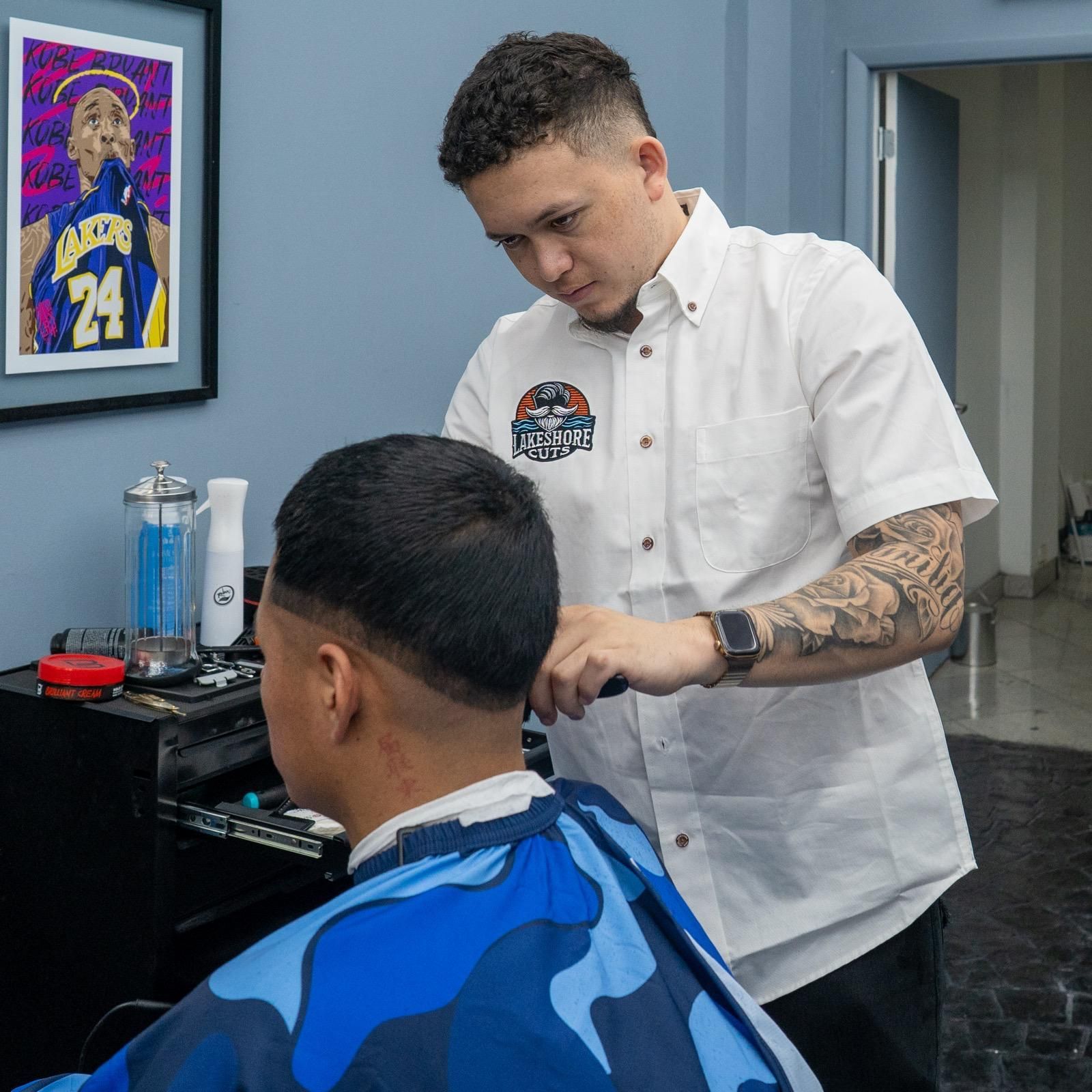 Barber cutting a client’s hair in a modern barbershop, with blue walls and framed art.