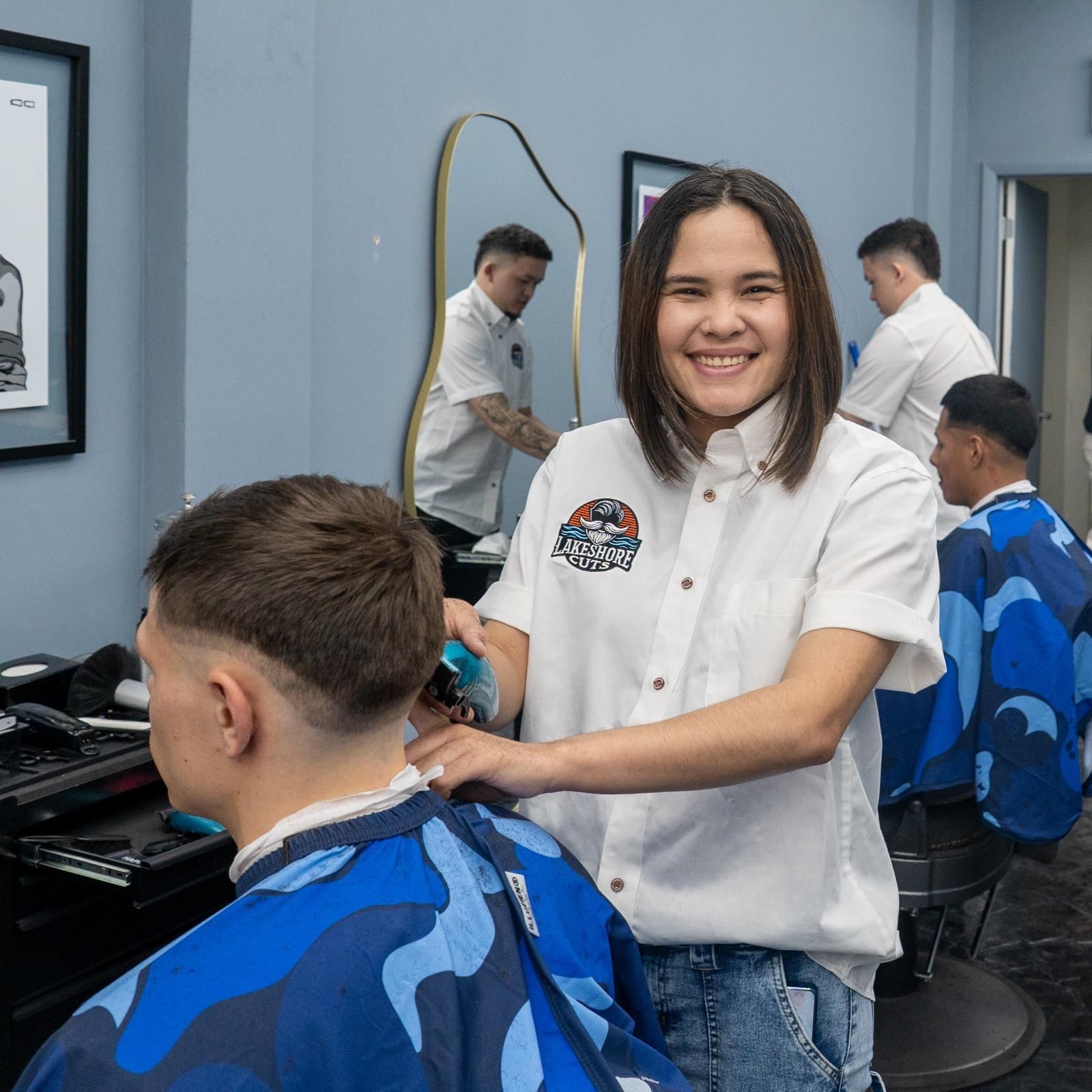 Hairdresser smiling while cutting a client’s hair in a salon with blue chairs and mirrors