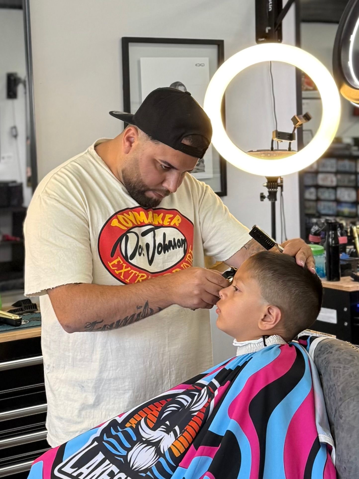 Barber trimming a client’s hair with clippers, client draped in colorful cape, in a shop setting
