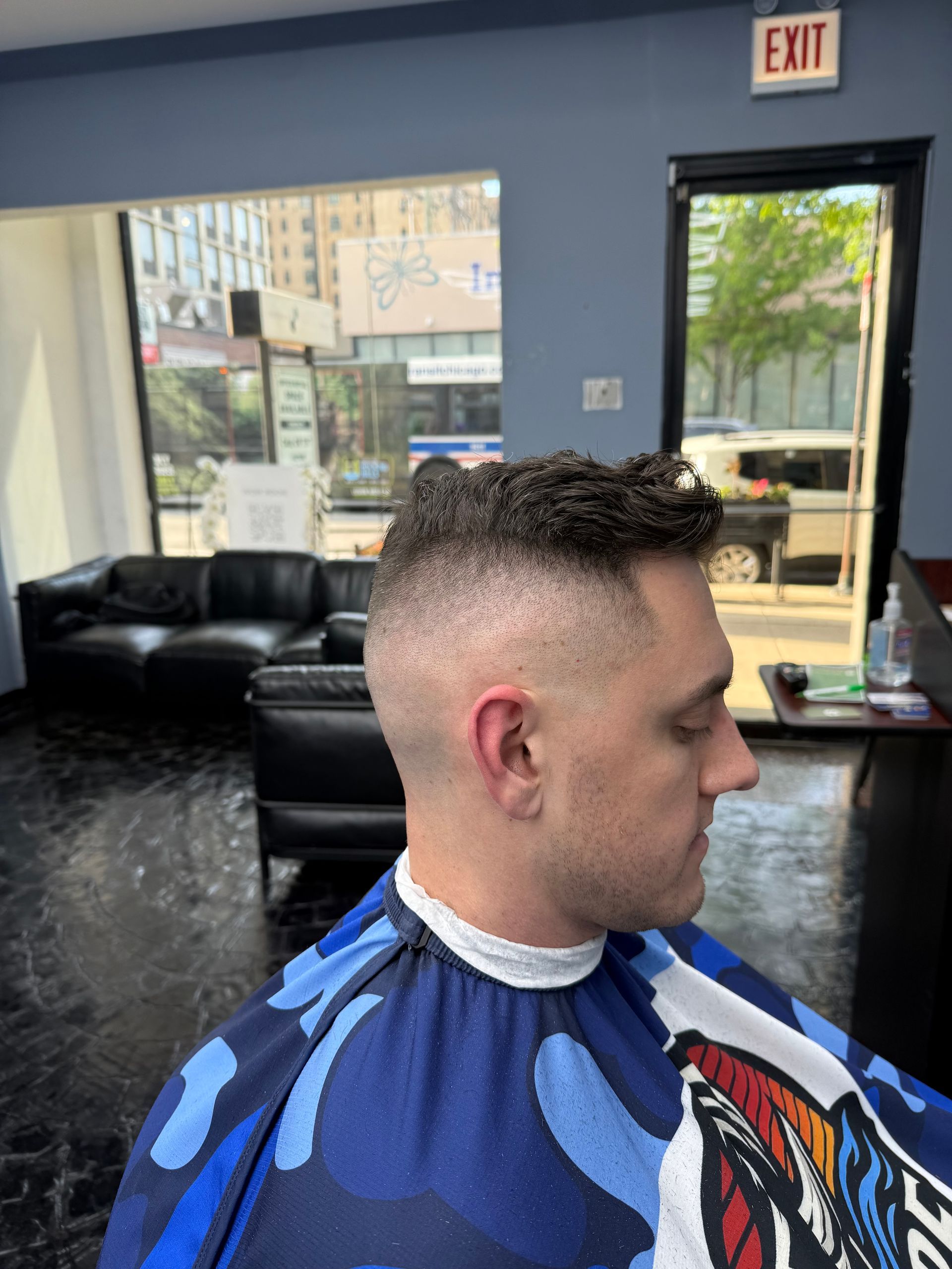 Man in a blue barber cape sitting in a salon chair with a short fade haircut