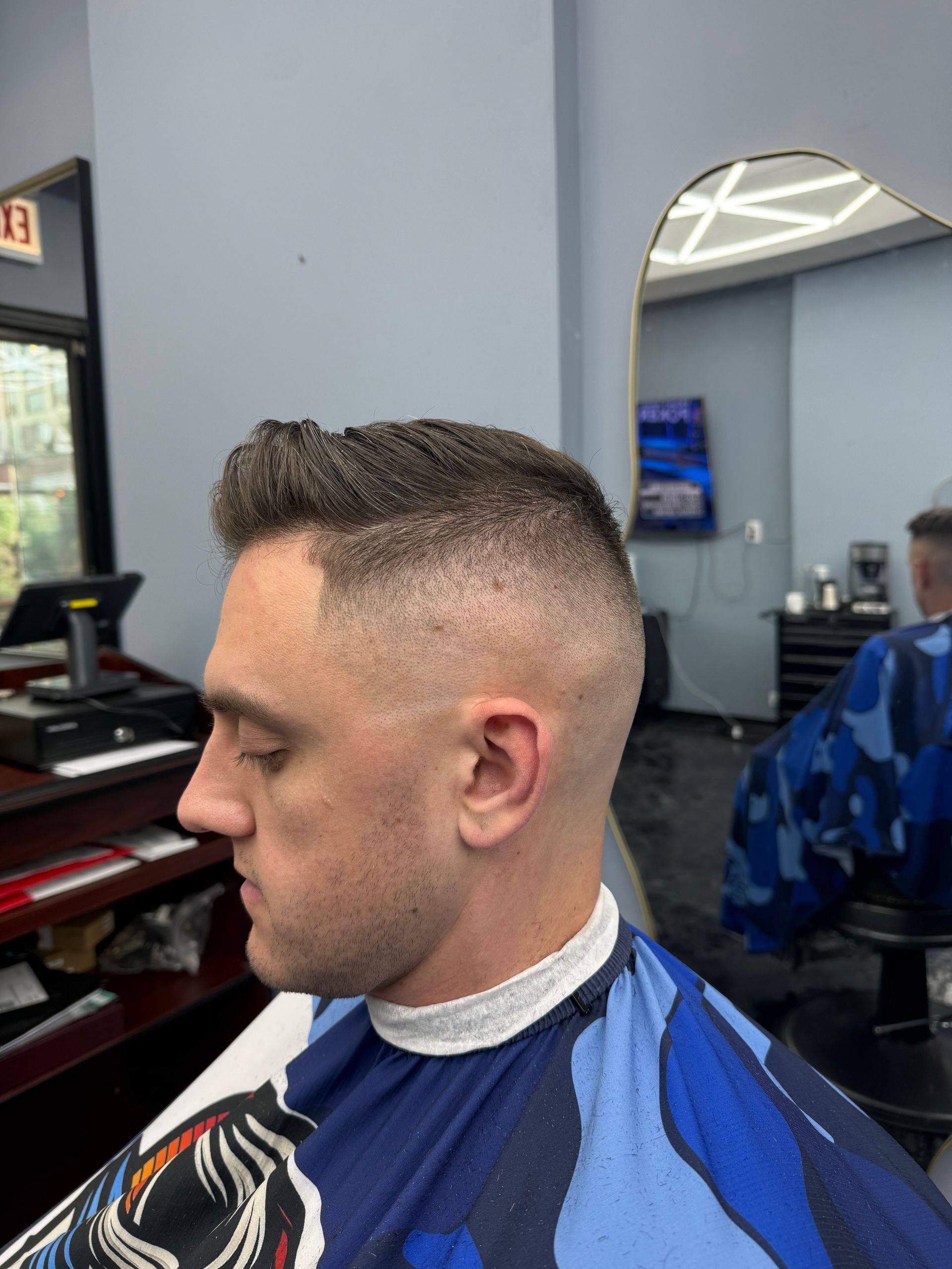 Man in a barbershop with a close fade haircut, wearing a blue cape, seen in profile.