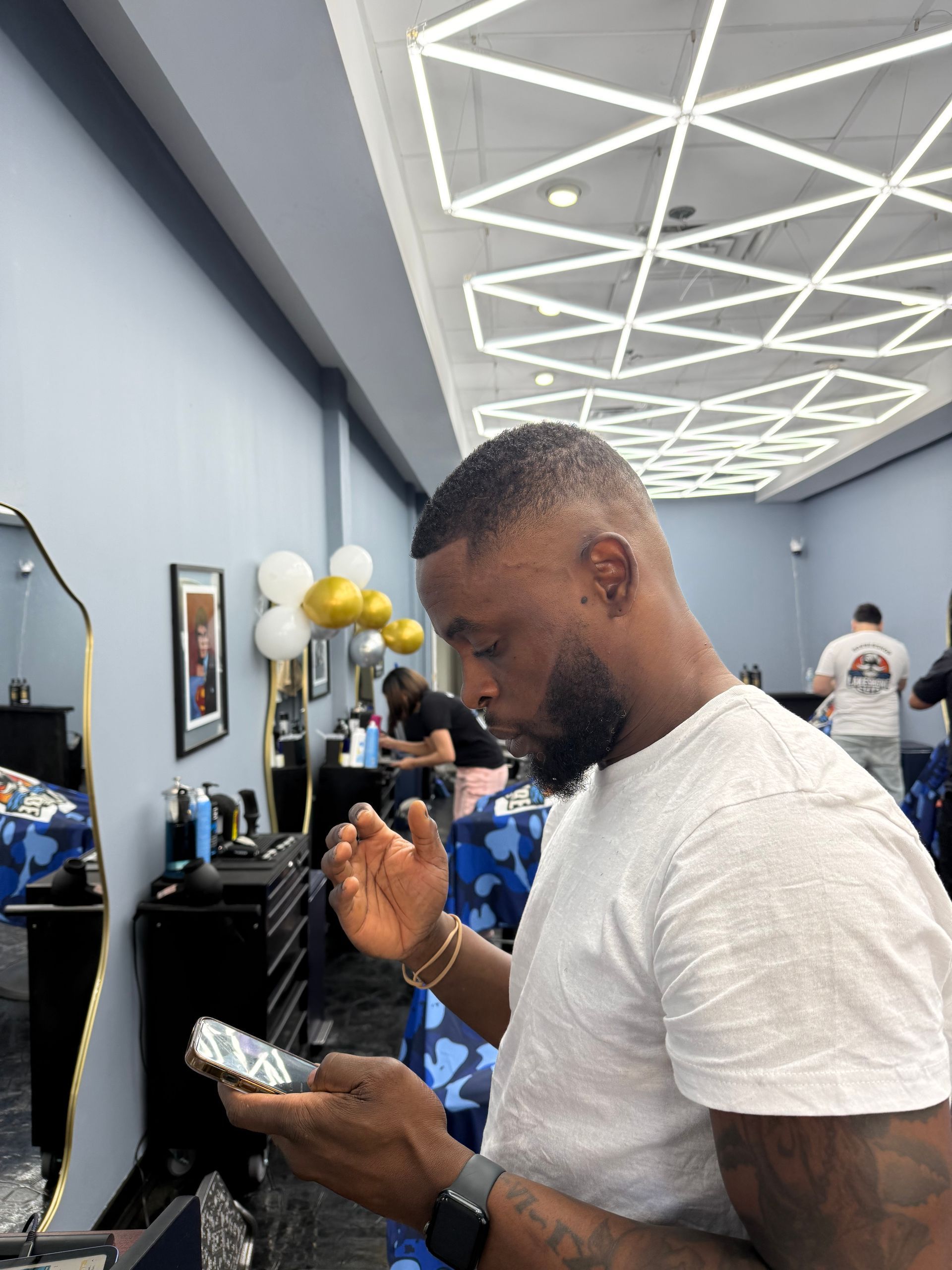 Man in a barbershop checking his phone beside a mirror and balloons
