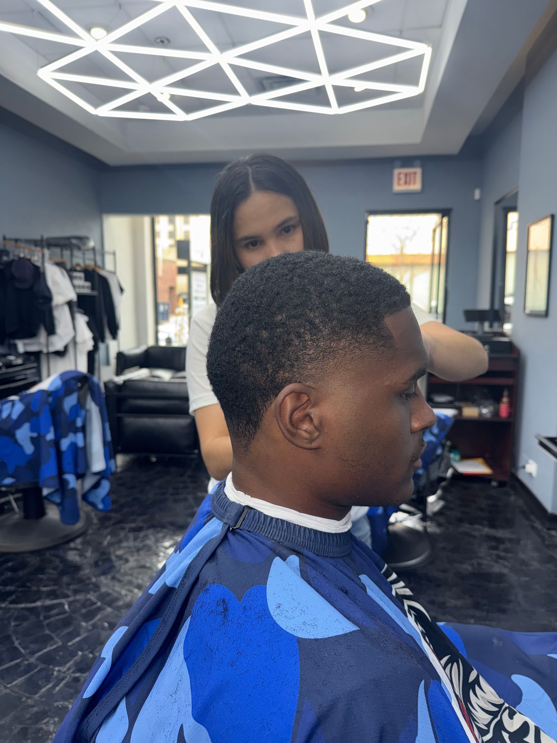 Barbershop haircut in progress, with a client in a blue cape and stylist behind him.