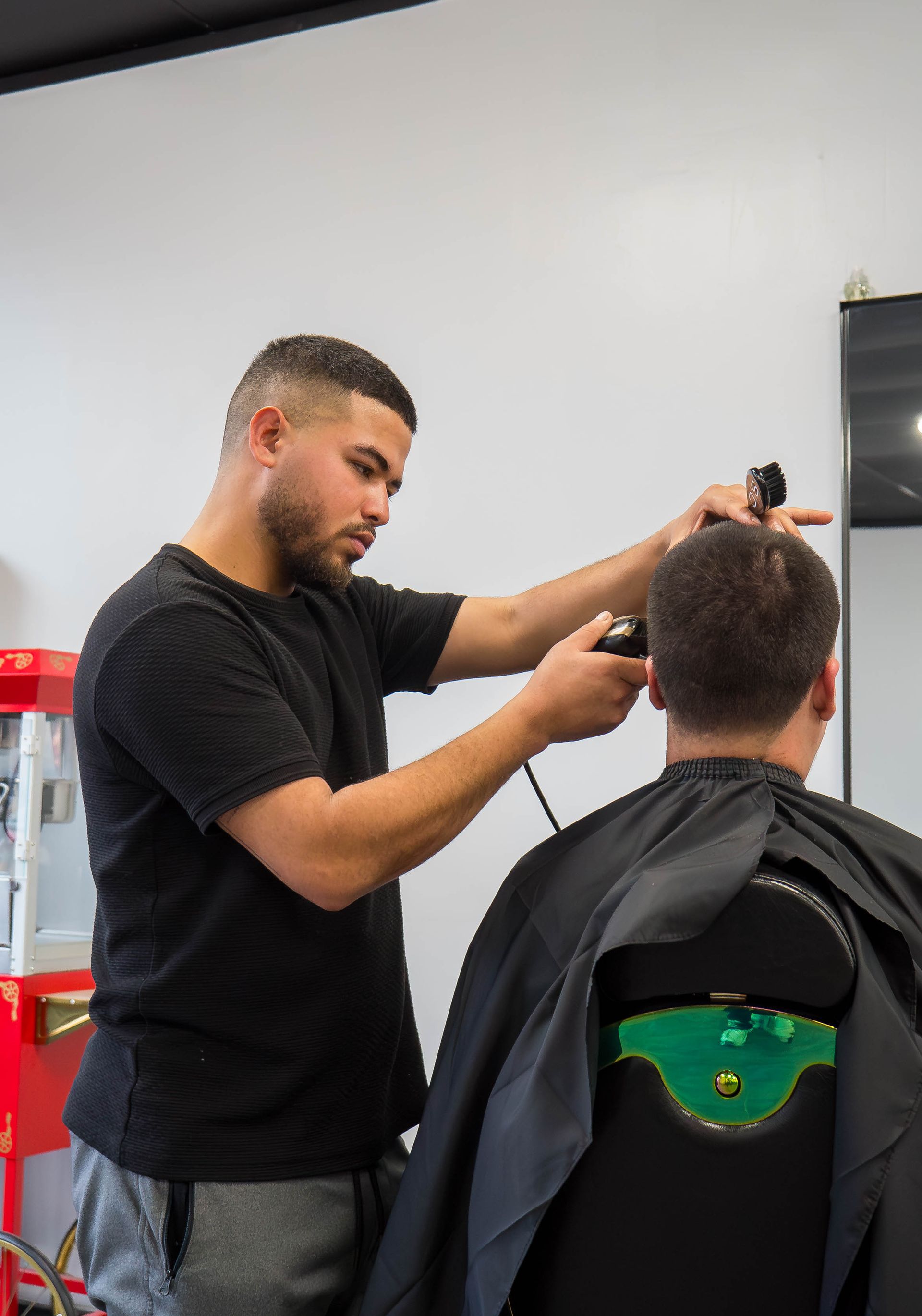 Barber cutting a client’s hair in a salon, with black cape and mirror visible.