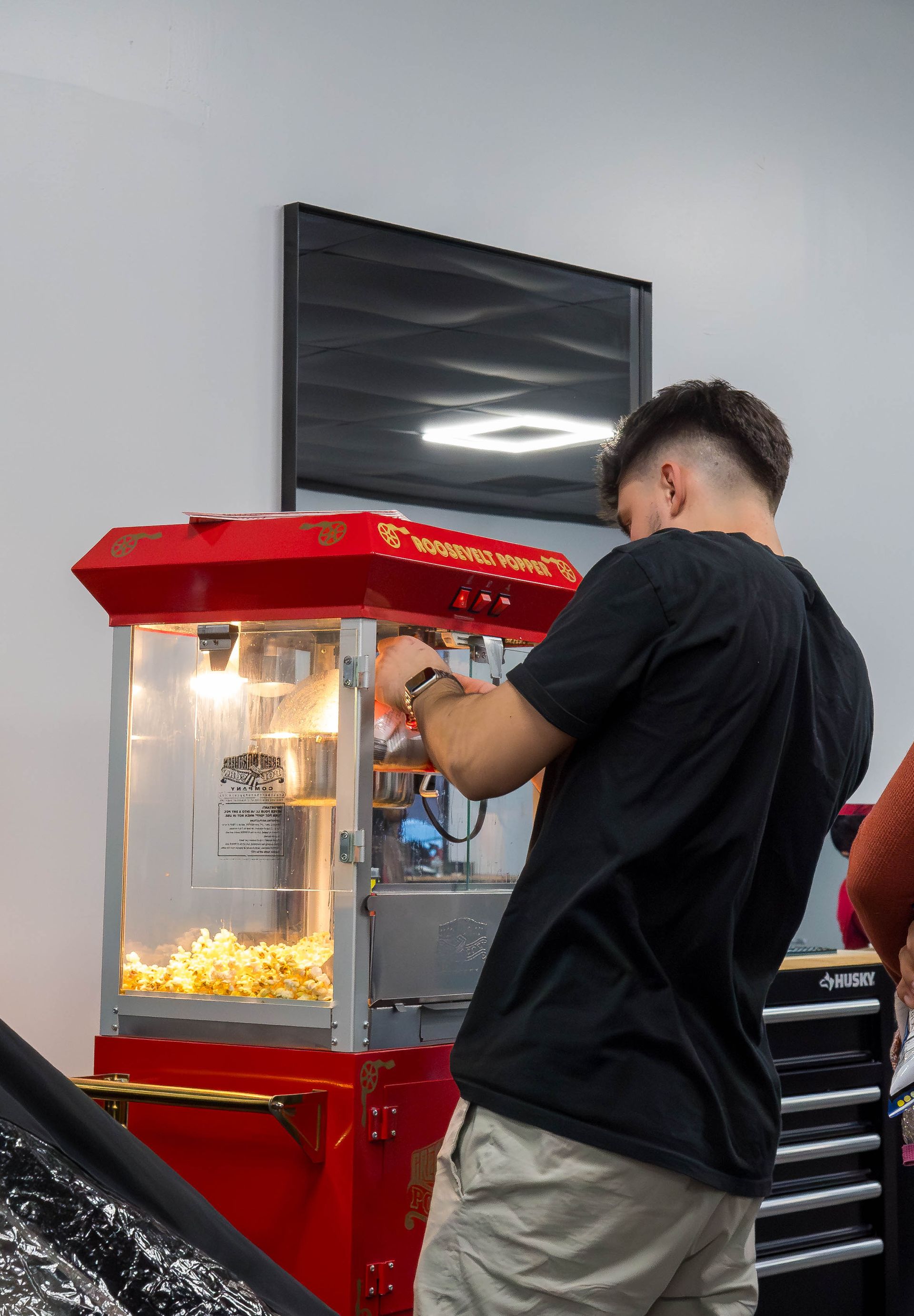 Man in a black shirt buying popcorn at a red concession stand under bright indoor lights