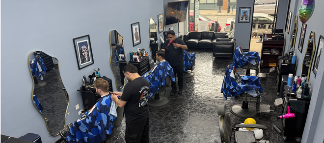 Barbershop with blue chairs and mirrors; a barber cuts a customer's hair near the entrance.