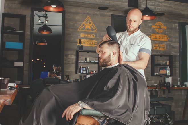 Barber in a vintage shop trims a seated client’s hair and beard.