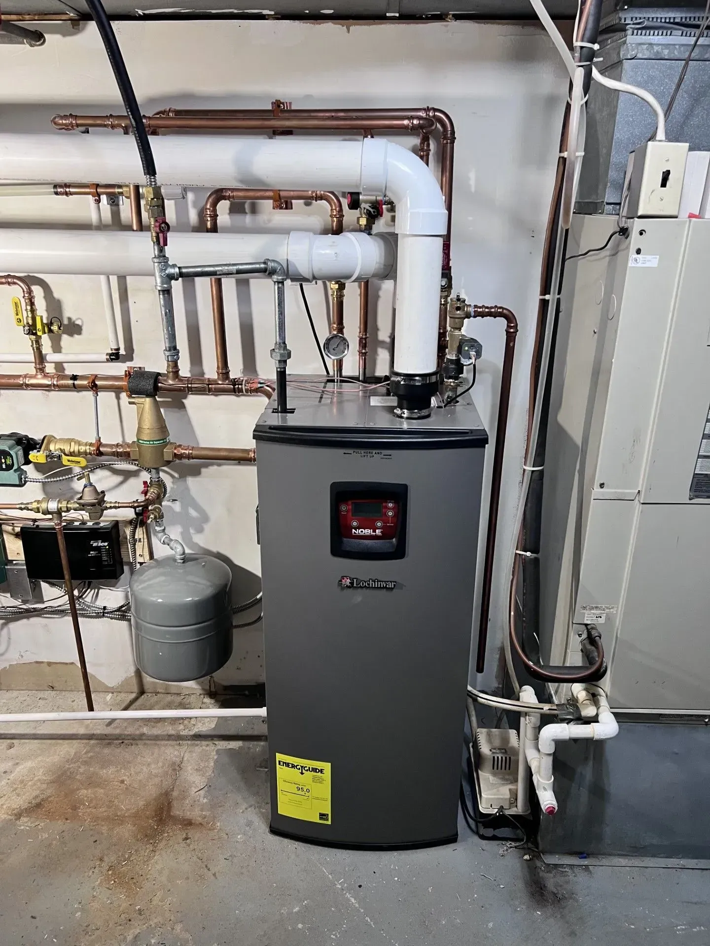 Gray water heater in a utility room with copper pipes and a control panel on the front