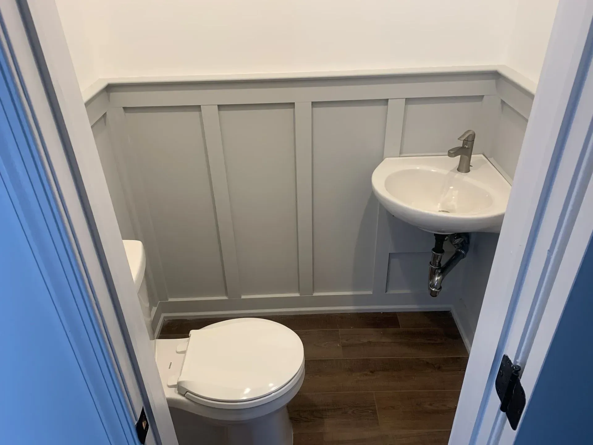 Small bathroom with a toilet, corner sink, gray wainscoting, and dark wood floor.