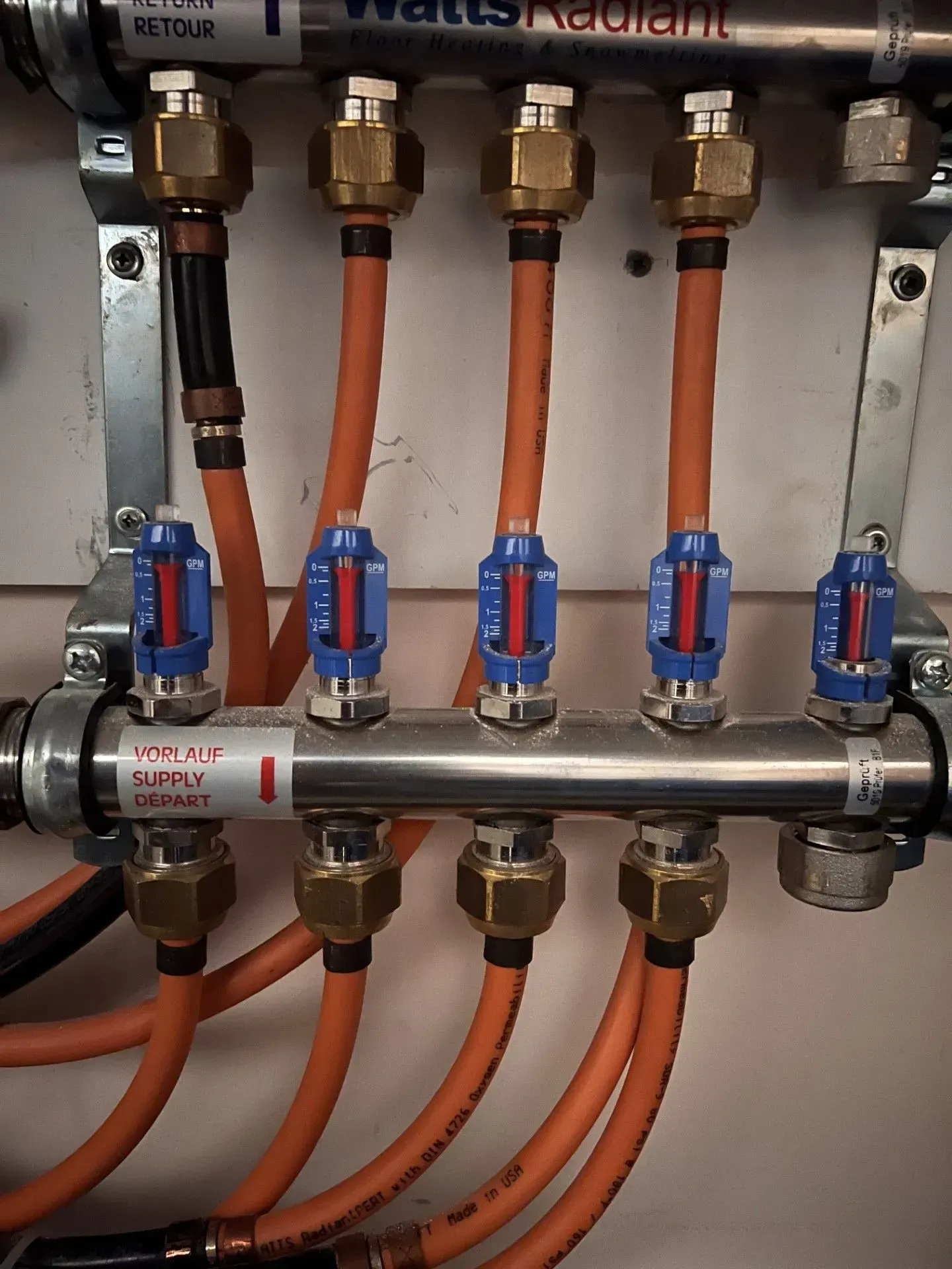 Close-up of a manifold with orange pipes and blue shutoff valves in a utility room