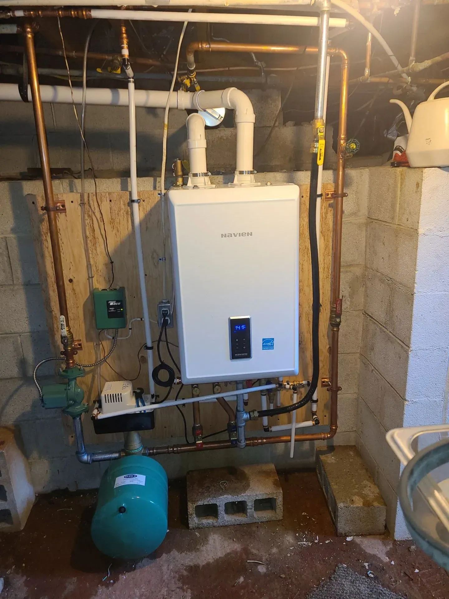 Basement utility room with a wall-mounted boiler, pipes, water tank, and exposed plumbing.