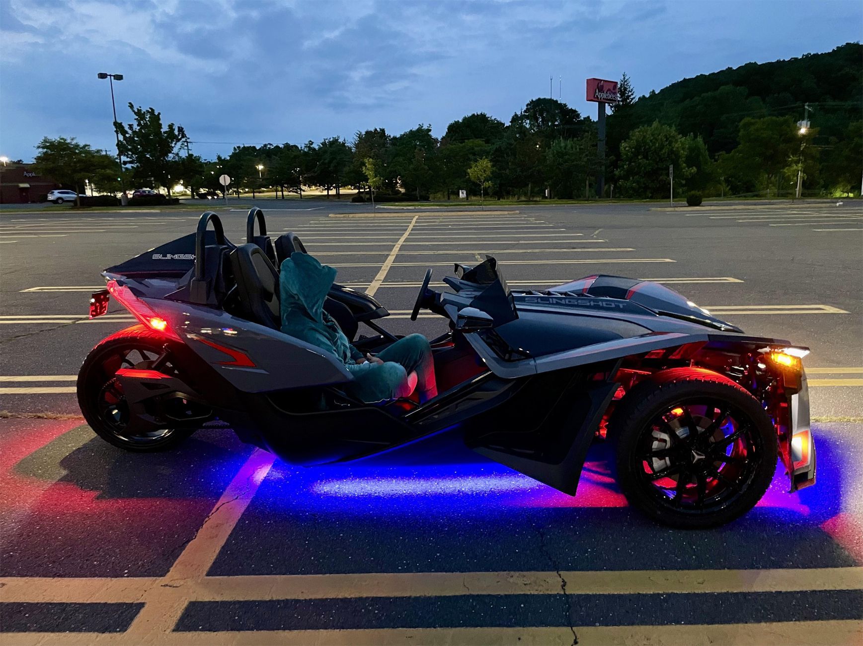 A slingshot is parked in a parking lot at night.